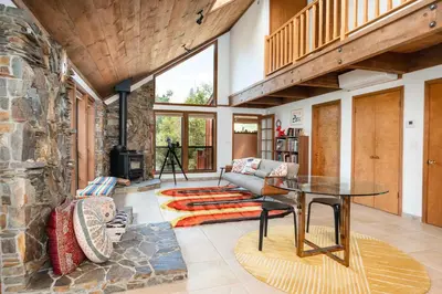 a living room with a table and a stone wall at Happy Days Retreat with Private Pool in Bass Lake Annex