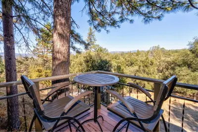a table and chairs on a deck with trees at Spacious Mountain View Home - Pool, Spa & Game Rm in Oakhurst