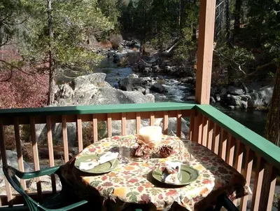 a table with a candle on a balcony with a river at Spacious Riverfront Cabin Rental Perfect for Large Groups near Sonora, California in Strawberry