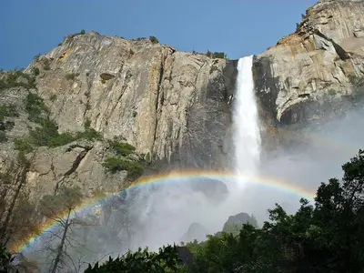 a rainbow over a waterfall in front of a mountain at Cozy Riverside Cabin Rental with Easy Access to Chilnualna Falls in California in Wawona