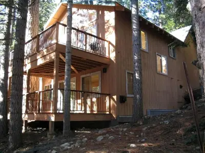 a large wooden house with a balcony in the woods at Exceptional Riverside Cabin Rental in the Trees near Pinecrest Lake, California in Strawberry