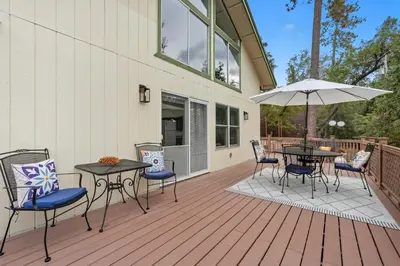 a deck with tables and chairs and an umbrella at Bearfoot Cabin 15 Min to Yosemite Gate! in Oakhurst