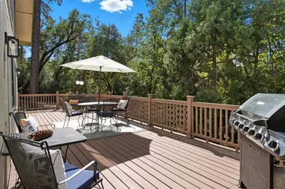 a deck with a grill and a table with an umbrella at Bearfoot Cabin 15 Min to Yosemite Gate! in Oakhurst
