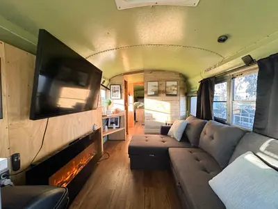 a living room in an rv with a couch and a tv at The Magic Skoolie in Visalia