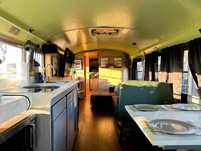 a kitchen in an rv with a sink and a table at The Magic Skoolie in Visalia
