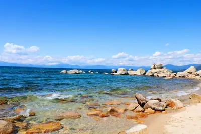a beach with rocks and the ocean on a sunny day at Chamberland Getaway Lake Views with Deck in Tahoma