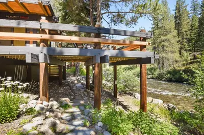 a wooden bridge over a river next to a building at Joy on the River Stunning Waterfront Home for 10 in Olympic Valley