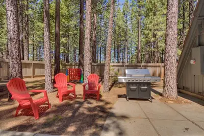 a patio with red chairs and a grill in the woods at Heavenly Hollow in South Lake Tahoe