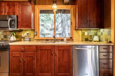 a kitchen with wooden cabinets and a sink and a window at Walk to Lake West Shore Cabin Hot Tub DogOK EVplug in Homewood