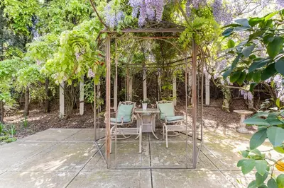 a table and chairs under a pergola with purple wisteria at Rose Garden in Sacramento