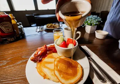 a person pouring syrup onto a plate of breakfast food at Stovepipe Wells Village in Death Valley