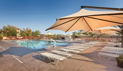 a pool with lounge chairs and a large umbrella at Wyndham Angels Camp 2BR Apartment with Resort Access in Angels Camp