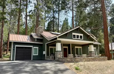 a green house with a garage in the woods at Black Bear Bungalow in White Wolf