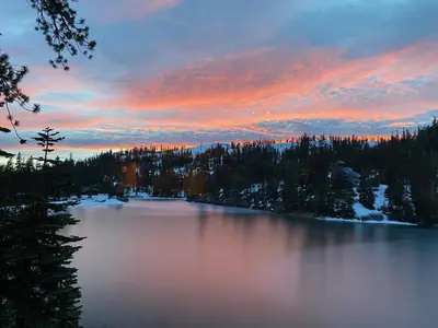 a view of a lake at sunset with trees and snow at The Lake Chalet in Bear Valley