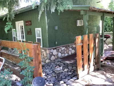 a green house with a wooden fence in front of it at Shady Creekside Cabin in Miramonte