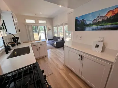 a kitchen with white cabinets and a living room at Tiny Blanca at Yosemite Gateway in Groveland