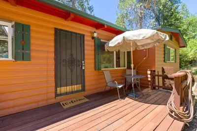 a house with a wooden deck with a table and an umbrella at Red Cabin in Twain Harte - King bed in Twain Harte