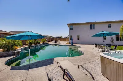 a swimming pool with two umbrellas and a table and chairs at 1 Mi to Golf! Spacious and Modern Home in Dinuba in Dinuba