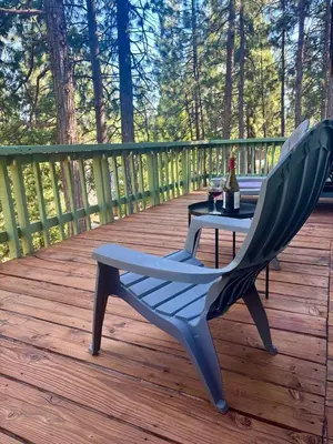a chair and a table on a deck with a bottle of wine at Woodland Chalet Retreat with Hot Tub in Arnold