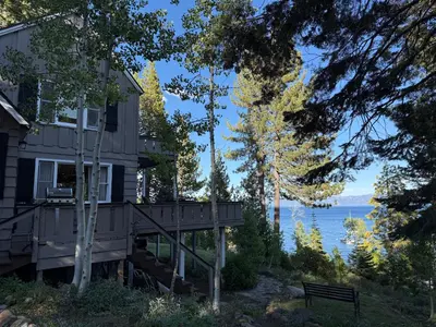 a house with a deck next to a body of water at Lake Tahoe Cabin I Hammocks, Paddle Boards and Bikes in Homewood