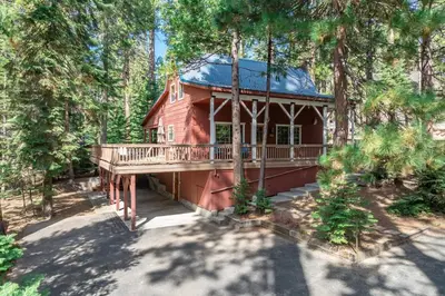 a red house with a deck in the woods at Dogwood Star Star Location Cozy Vibes in Shaver Lake