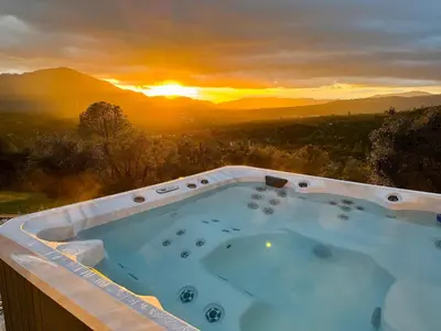 a hot tub with a sunset in the background at Relax Under the Stars, Best view in town , Yosemite House with Firepit, Hot Tub, Game Room & Pool table in Oakhurst