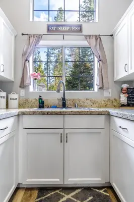a kitchen with white cabinets and a sink and a window at Halonas Cozy Cabin 2M To Lake in Shaver Lake