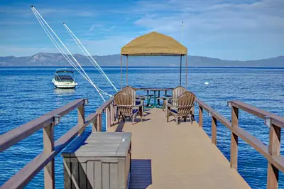 a dock with chairs and a boat on the water at Lake Tahoe West Shore Lake Front 5 bedroom Cabin in Homewood