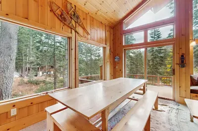 a dining room with a wooden table and large windows at Bear Creek Pond Chalet in Alpine Meadows