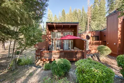 a cabin in the woods with a deck and an umbrella at Ridge Court # 13 by Tahoe Getaways - 3BR Palisades at Alpine Condo w Ski Shuttle & Tennis! in Alpine Meadows