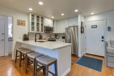 a kitchen with white cabinets and a counter with bar stools at Mammoth Mtn Ski-InandOut Condo with Hot Tub Access! in Mammoth Lakes