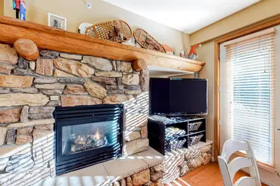 a stone fireplace in a living room with a tv at Mammoth Green 116 in Mammoth Lakes