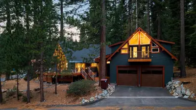 a blue house with a garage in the woods at Retreat with Lake Access Deck Modern Interior Agate Peak by Avantstay in Carnelian Bay