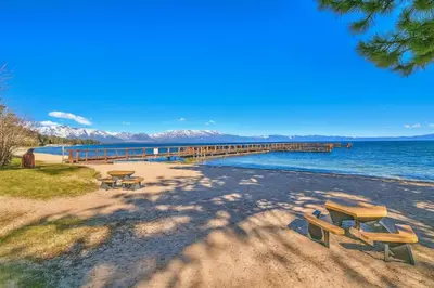 a beach with two picnic tables and a dock at Lakefront Townhome in South Lake Tahoe in South Lake Tahoe