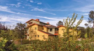 a large yellow house on a hill with trees at Wyndham Angels Camp- 1 BR- Apartment with Resort Access in Angels Camp