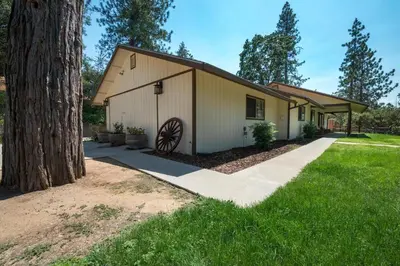 a house with a tree next to a sidewalk at Blue Bird Ranch in Oakhurst