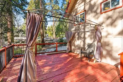 a wooden deck with a chair and curtains on it at Smoke Tree-Newly Updated Family Retreat in Shaver Lake