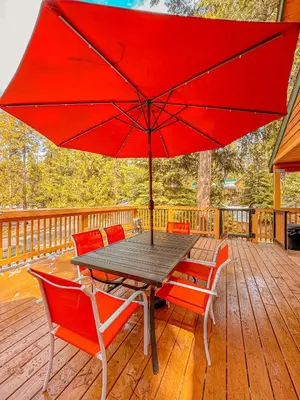 a table with chairs and a red umbrella on a deck at Bear Bottoms Family Cabin-Huge GAME ROOM in Shaver Lake