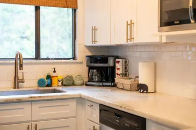 a kitchen with white cabinets and a black cat sitting on the counter at Kamp Kokanee-Updated Condo Near Spa Sauna in Shaver Lake