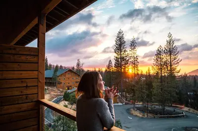 a woman standing on a balcony looking out at the sunset at Rush Creek Lodge at Yosemite in Groveland