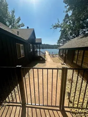 a house with a fence next to a body of water at Boat Dock - Lake Front - Dog Friendly - Sleeps 7 in Bass Lake
