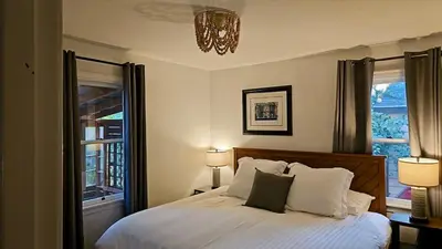 a bedroom with a bed with two windows and a chandelier at Amador Wine Country Cottage in Fiddletown