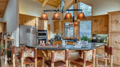 a kitchen with wooden cabinets and a large island with bar chairs at Truckee Mountain Cabin with Hot Tub Game Room Forest Views Gray Wolf Lodge by AvantStay in Truckee