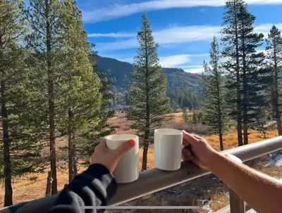 a person holding two cups of coffee on a railing at The Meadows- Charmed Ski & Relax Studio in Kirkwood