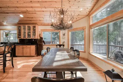 a dining room with a wooden table and windows at Kindred Pines at Tahoe Donner by Tahoe Getaways - 3BR with Pool Table & HOA in Truckee