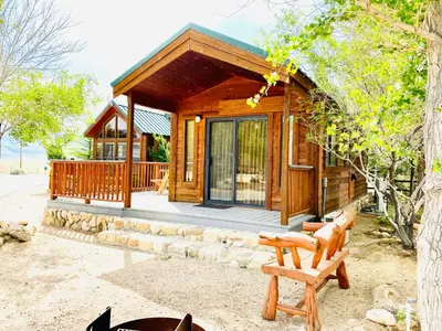 a wooden cabin with a bench in front of it at Boulder Creek RV Resort in Lone Pine