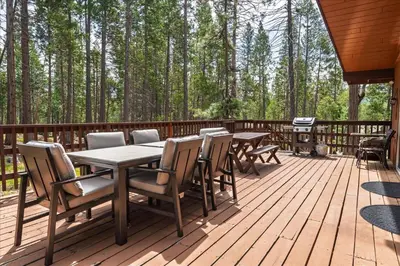 a wooden deck with tables and chairs and trees at PaPa Bear Cabin in North Wawona
