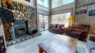 a living room with a stone fireplace and a table at Summit 110 Apartment in Mammoth Lakes