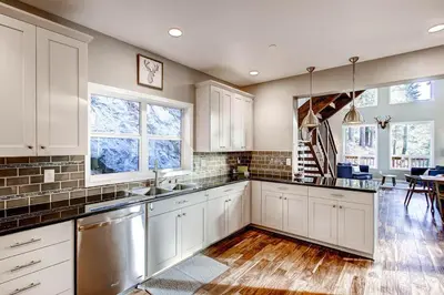 a kitchen with white cabinets and wooden floors and windows at Kildrummy Lodge in Yosemite West