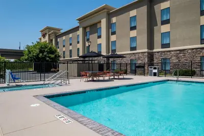 a swimming pool in front of a building with tables and umbrellas at Hampton Inn by Hilton Turlock in Turlock
